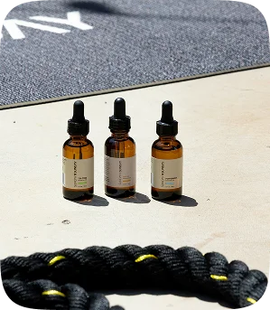 Three amber glass dropper bottles standing on concrete next to black gym ropes.